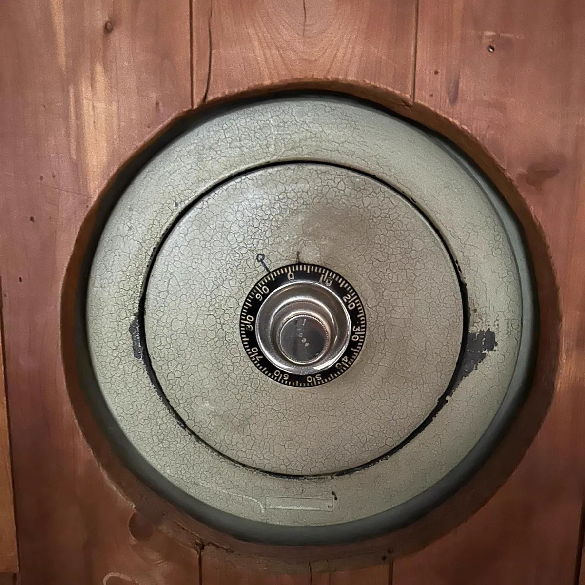 Antique round-door wall safe with combination dial set into wood paneling